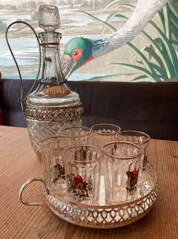 A vintage decanter with matching tray housing six fluted glasses featuring various hunting scenes.