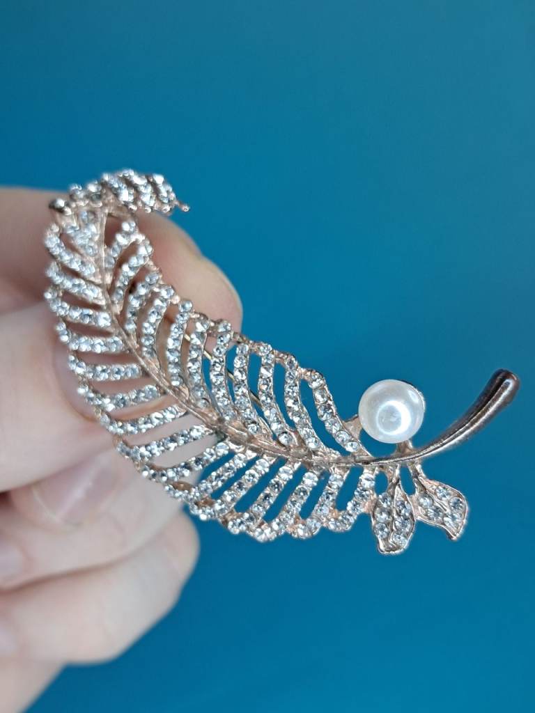 Vintage gold-tone metal feather brooch decorated with clear crystals and a single faux pearl. 