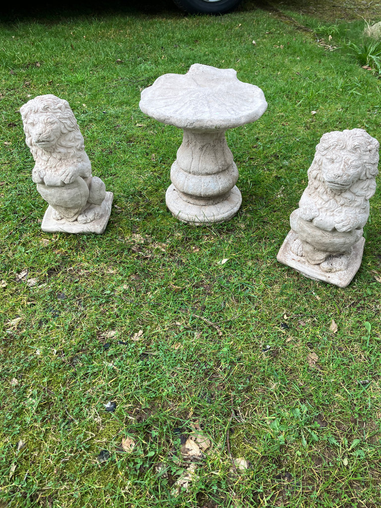 THREE STONE GARDEN ORNAMENTS TWO SITTING LIONS WITH SHIELDS AND A SHELL BIRD TABLE 