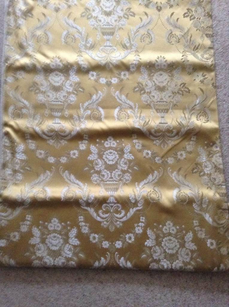 ROLL OF GOLDEN BROCADE MATERIAL WITH URN AND FLOWERS PATTERN.