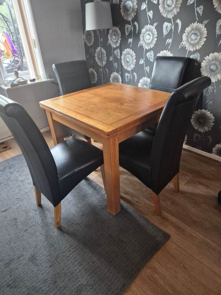 Solid wooden extendable dining table paired with 4 high-back black faux leather dining chairs 