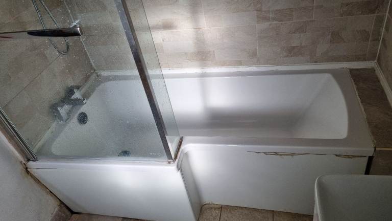 Bathroom tub wirh tap mixers, showers and glass screen.