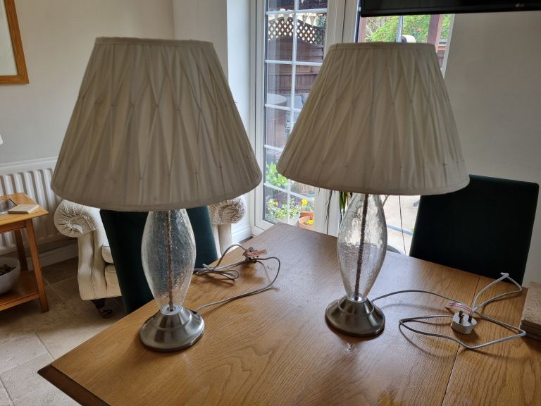 A pair of glass and metal lamps with cream shades
