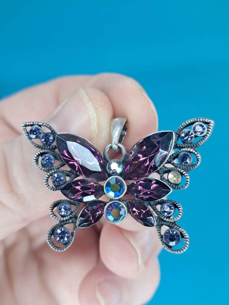Vintage-style butterfly pendant with purple and iridescent crystal rhinestones and a metal alloy....