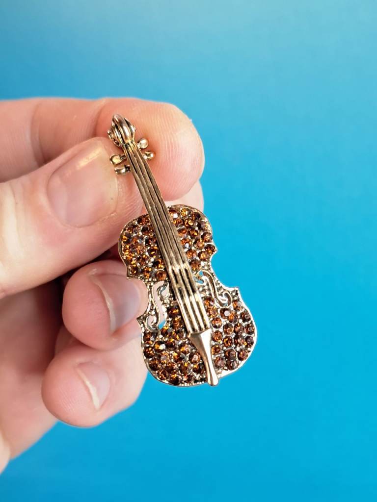 This is a gold-tone, rhinestone-encrusted violin brooch. 