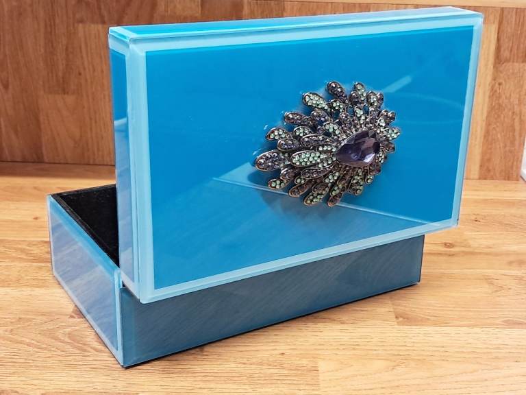 This is a blue mirrored glass square jewellery box with a crystal flower decoration. 