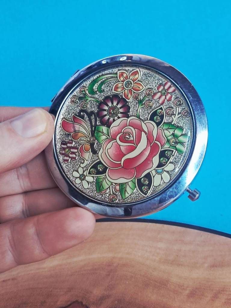 vintage-style metal compact pocket mirror with a floral and butterfly design. 