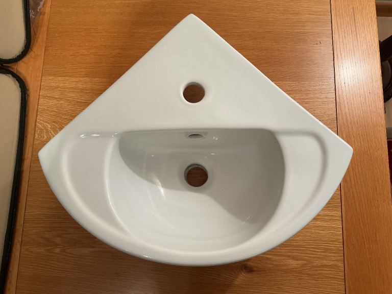 This is a white wall-mounted ceramic corner washbasin, previously installed, clean and pristine.