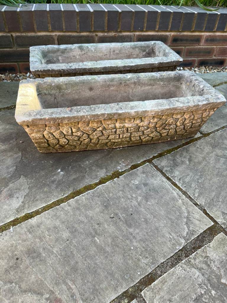 Two identical stone trough planters with wall effect on outer surface.