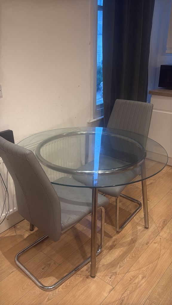 Modern glass dining table with two comfortable grey faux-leather chairs.