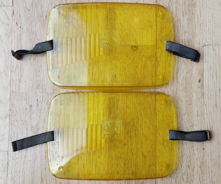 A pair of vintage Lucas 7 x 4.5 inch amber plastic headlamp beam deflectors with elastic fasteners