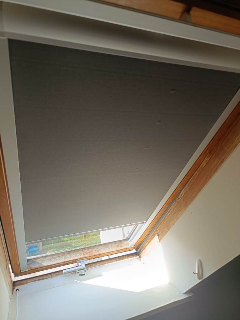 A blackout blind designed for a Velux window, in good working order. It's a grey fabric roller blind