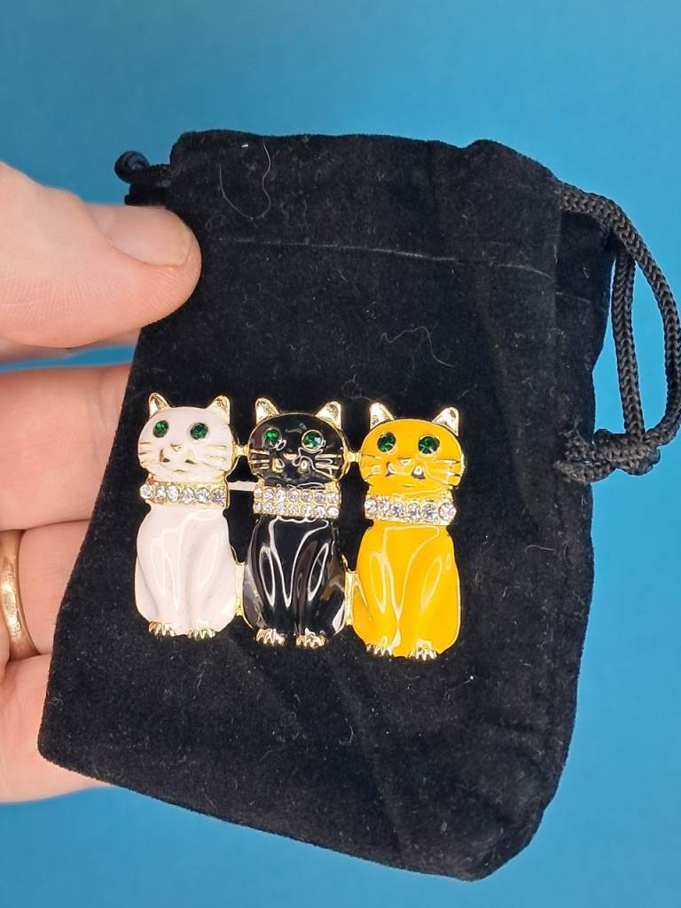 gold-tone metal brooch featuring three cats (white, black, and orange)
