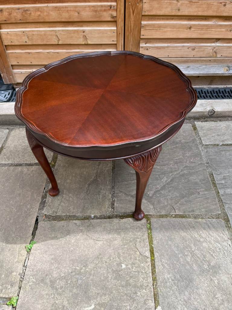 A round dark brown wooden coffee table with four cabriole legs.