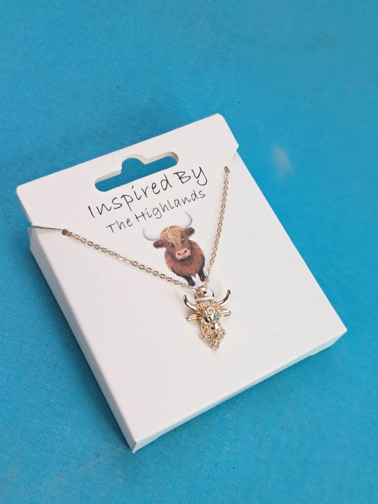 Gold-toned Highland cow necklace packaged on a card titled "Inspired By The Highlands".