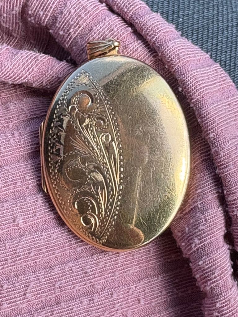 vintage oval locket made of rolled gold, featuring a classic etched or engraved pattern on its front
