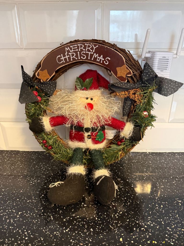 Santa Claus Christmas wreath featuring a plush Santa figure and a "Merry Christmas" sign. 14"  