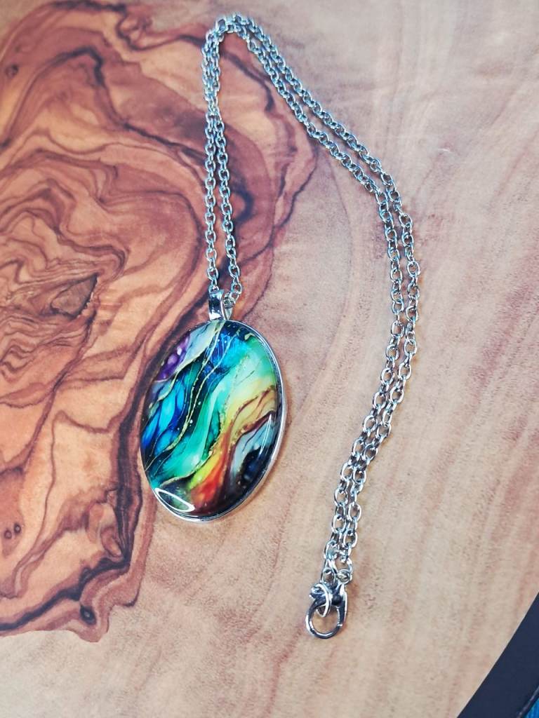 This is a multi-coloured oval glass cabochon necklace with a silver-toned chain
