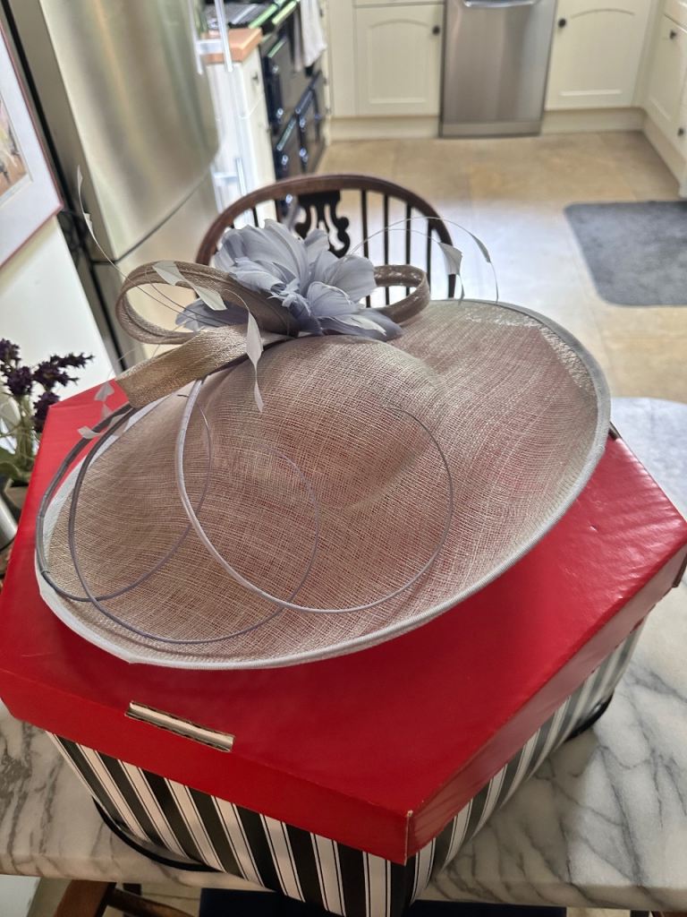 This hat is a neutral beige with elegant lilac feather and ribbon details