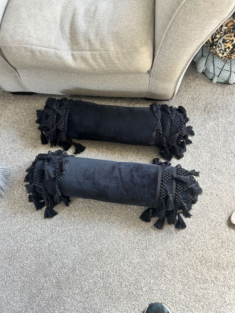 Two black tassel bolster cushions 