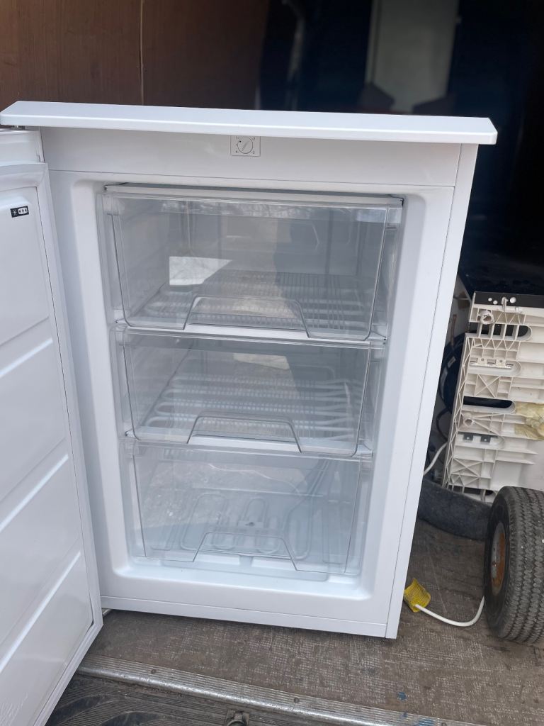 Small white freestanding freezer with three clear drawers.