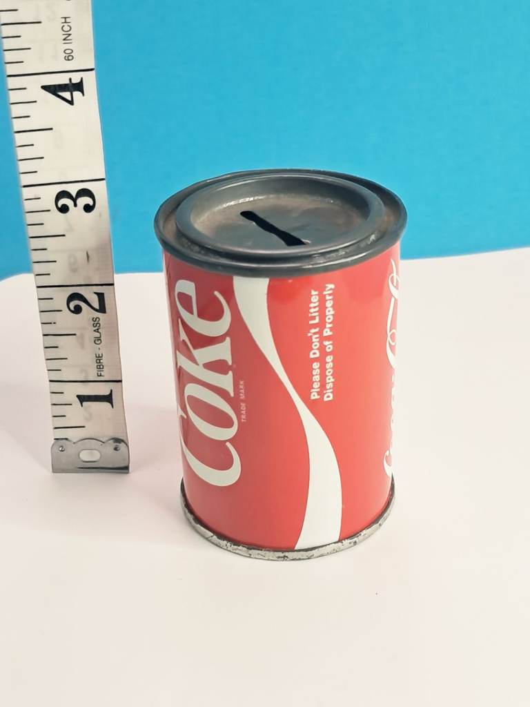 Vintage Coca-Cola branded tin can money bank, likely from the 1970s or 1980s. 