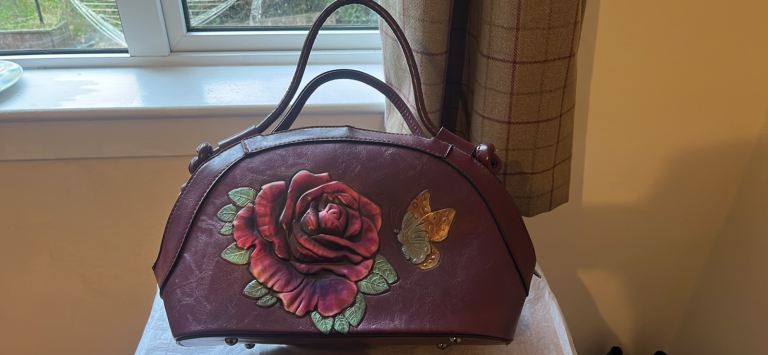 The handbag is a vintage or vintage-style item characterized by its embossed rose and butterfly desi