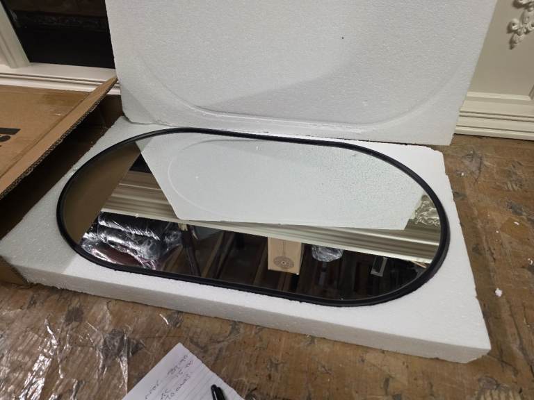 A new still boxed black metal framed oval shaped wall mounted mirror .